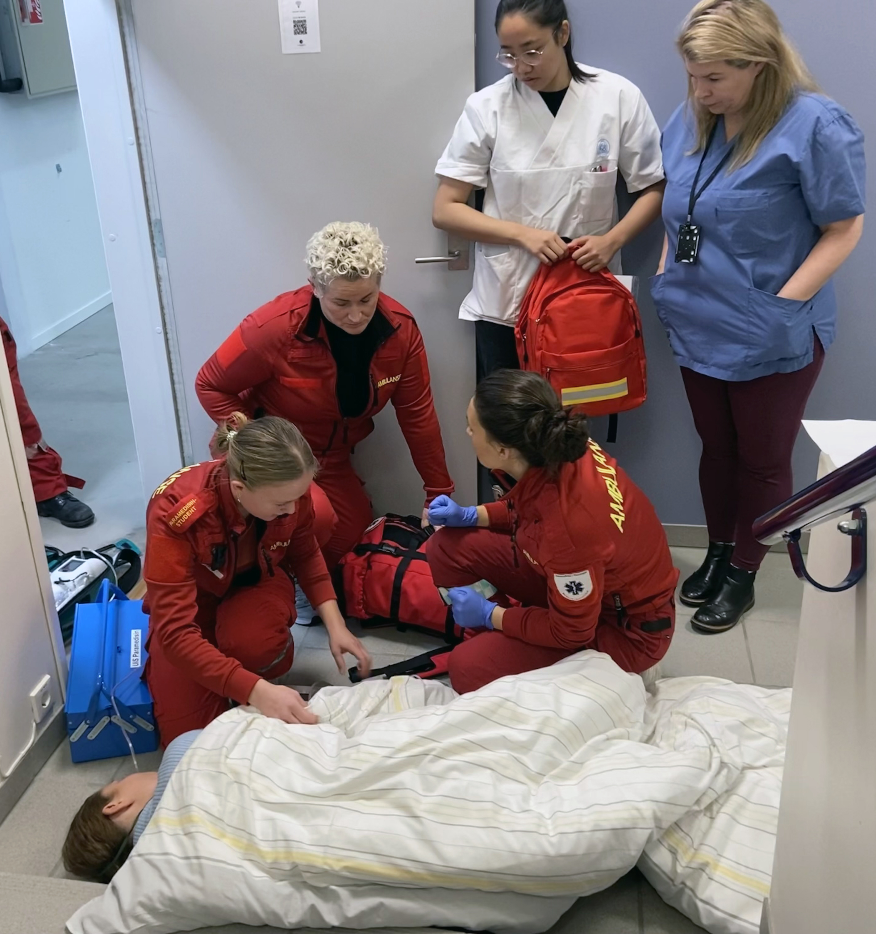 Tre kvinnelige paramedisinere og to kvinnelige sykepleiere som hjelper en pasient.